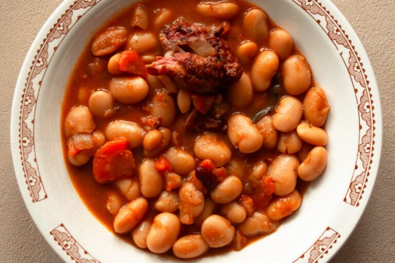 Wie bereitet man deftige Bohnen mit Speck und Tomatensoße zu?